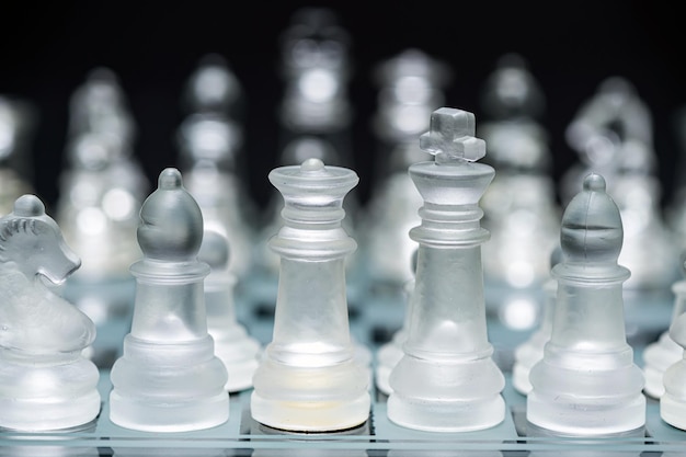 Glass transparent chess pieces on a checkerboard selective focus closeup isolated on black