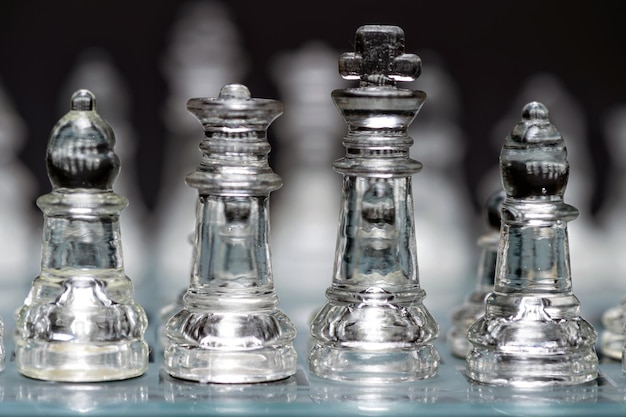 Glass transparent chess pieces on a checkerboard selective focus closeup isolated on black