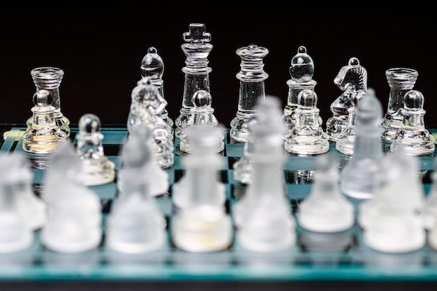 Glass transparent chess pieces on a checkerboard selective focus closeup isolated on black