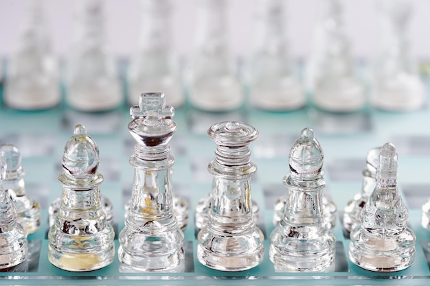 Glass transparent chess pieces on a checkerboard selective focus closeup isolated on light