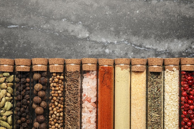 Glass tubes with different spices on grey marble table flat lay Space for text