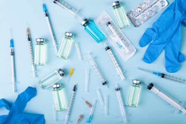 Glass vaccine, ampoules bottles, gloves, syringes needles and pills on blue background