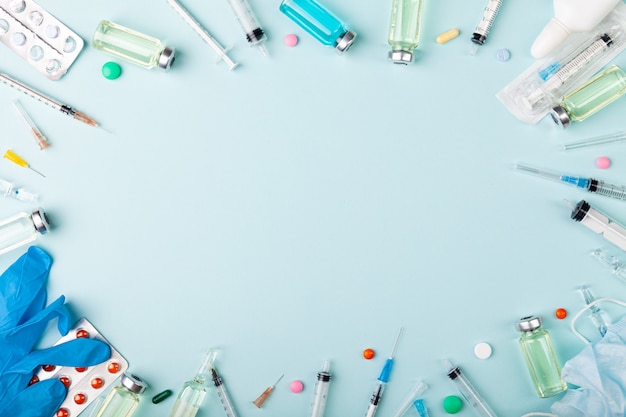 Glass vaccine, ampoules bottles, gloves, syringes needles and pills on blue background