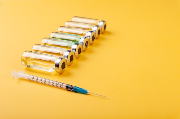 Glass vaccine, ampoules bottles, syringes and medicines on yellow background