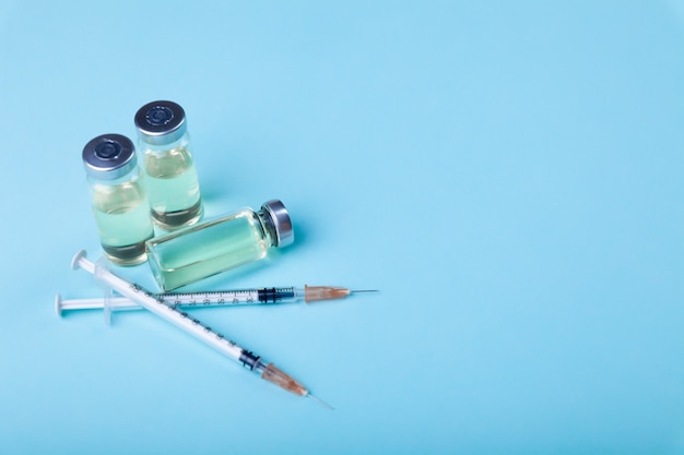 Glass vaccine ampoules bottles and syringes needles on light blue background