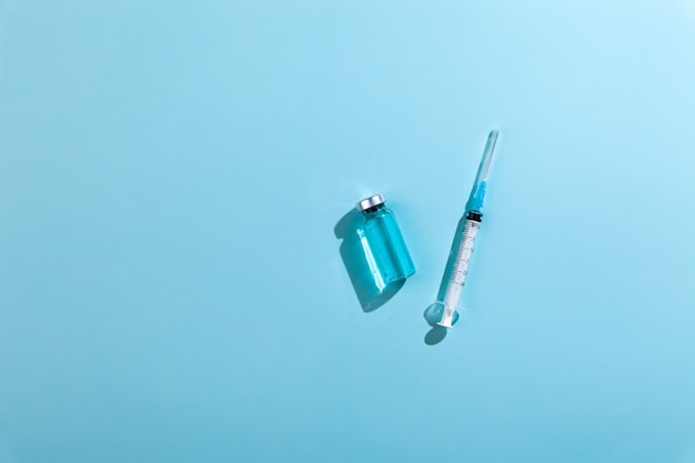 Glass vaccine bottle with syringe needle on blue background