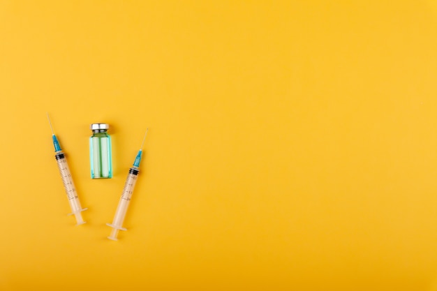 Glass vaccine bottle with syringe needles on yellow background