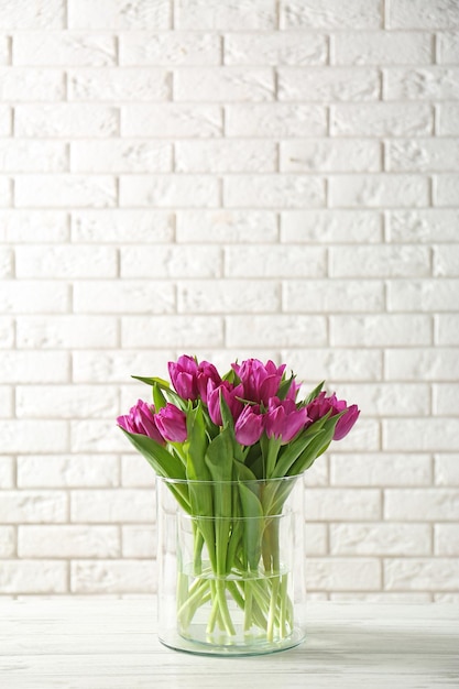 Glass vase with bouquet of beautiful tulips on brick wall background