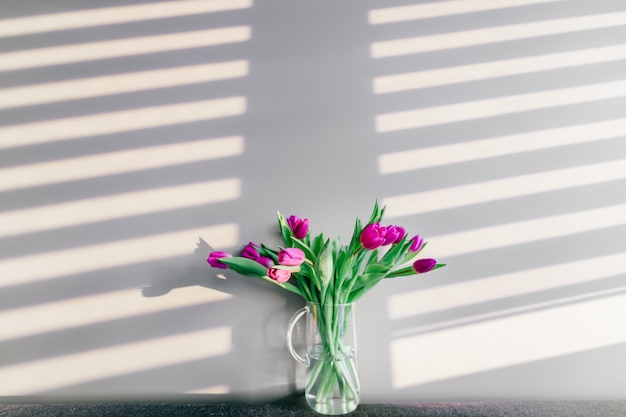 Glass vase with bouquet of beautiful tulips on grey wall