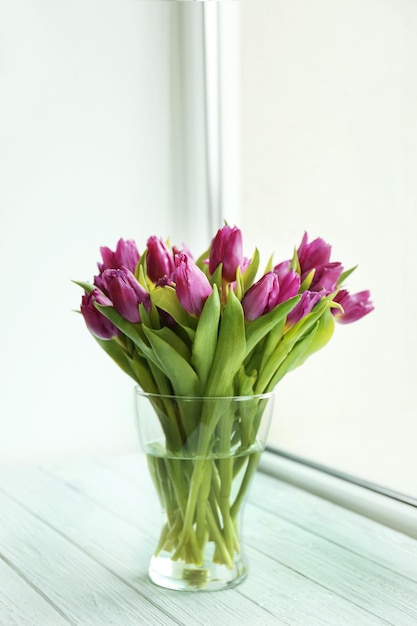 Glass vase with bouquet of beautiful tulips on windowsill