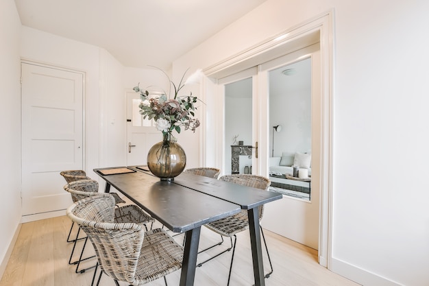 Glass vase with bunch of fresh flowers placed on table with chairs in stylish dining room at home