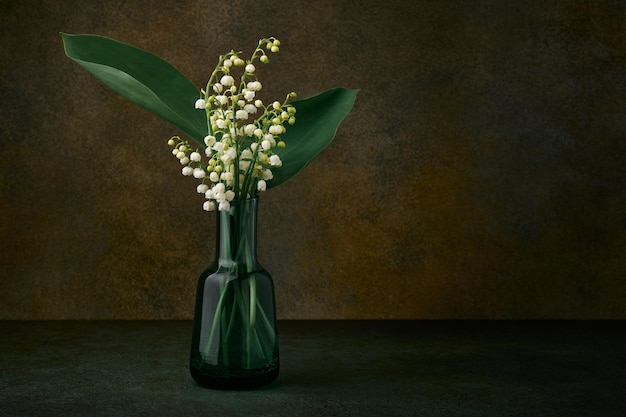 Glass vase with lilies of the valley on a dark background close up with copy space