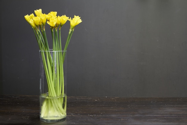 Glass vase with yellow daffodils on a dark wooden table, greeting background or concept