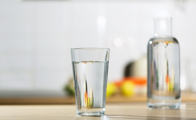 Glass of water is poured into a glass in a kitchen table