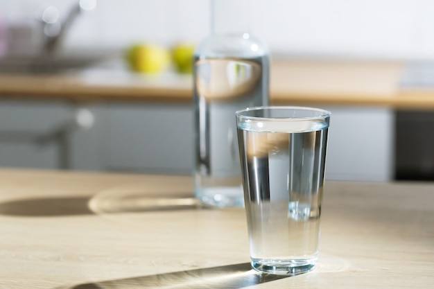 Glass of water is poured into a glass in a kitchen table