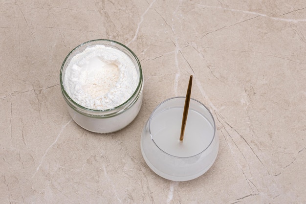 Glass of water and a jar of collagen goodnesson a marble beige background