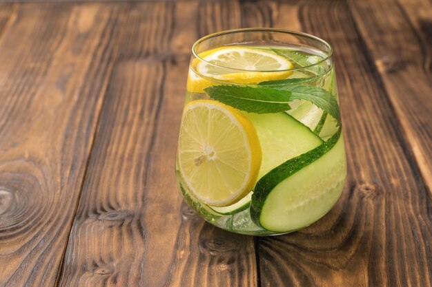 A glass of water and slices of lemon and cucumbers on a wooden table