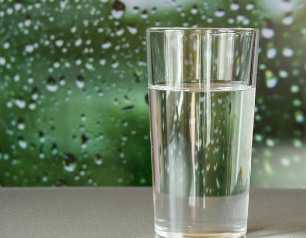 Glass of water stands on a blurred green background with drops