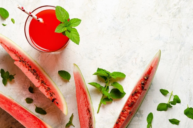 A glass of watermelon juice slices of watermelon fruit and mint leaves on a light background