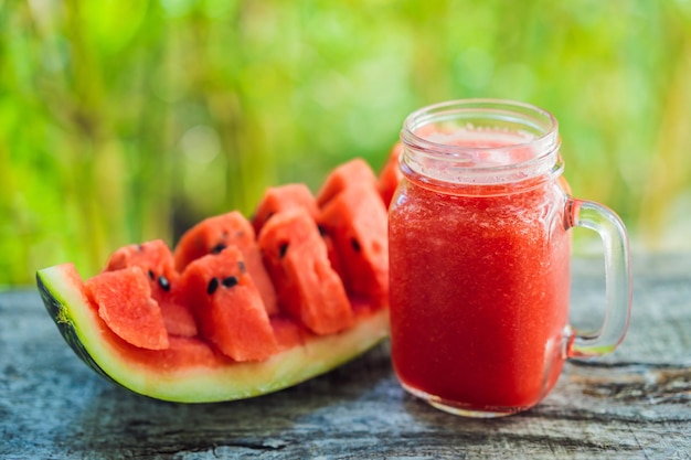 Glass of watermelon smoothie and a piece of watermelon on a wooden table