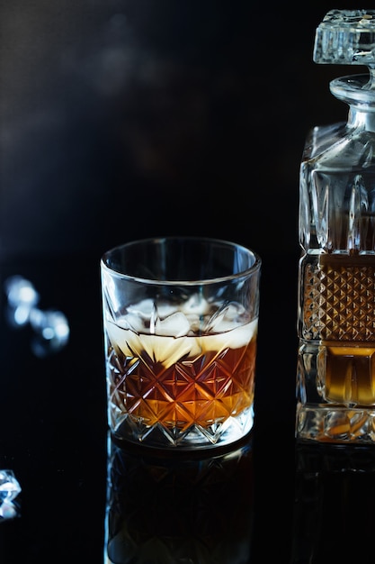 Glass of whiskey or bourbon with ice on black stone table.