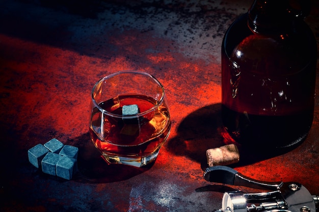 Glass of whiskey with decanter and chilling cubes viewed high angle in red light on an old counter in a pub