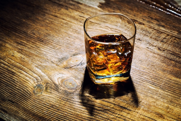 Glass of whiskey with ice cubes on wood table