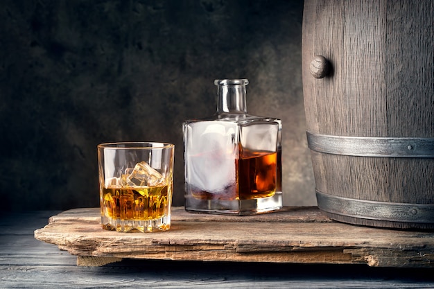 Glass of whiskey with ice decanter and barrel