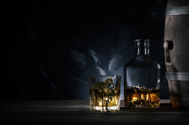 Glass of whiskey with ice, decanter and a wooden barrel