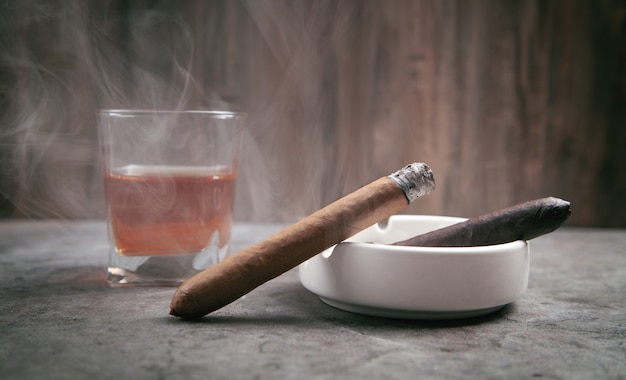 Glass of whisky, ashtray and cigars on the table.