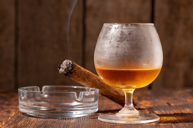 Glass of whisky and lighted cigar in an ash tray