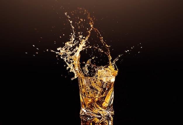 A glass of whisky with splashes from the ice cube