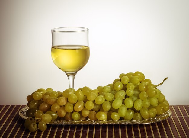 Glass of white wine and a bunch of green grapes on a metal dish