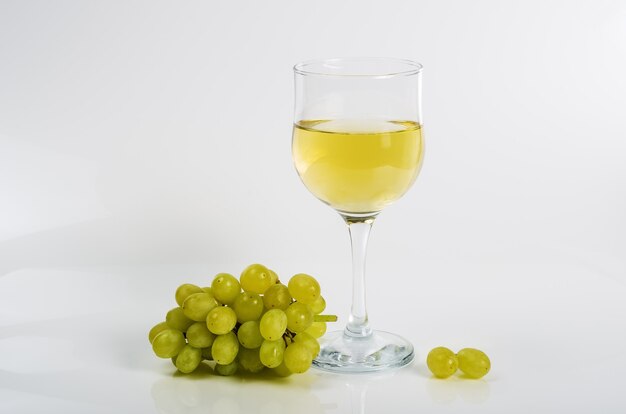 Glass of white wine and a bunch of green grapes on a white background