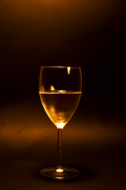 Glass of white wine on a dark background in golden tones glass of white wine on orange background with lights on glass