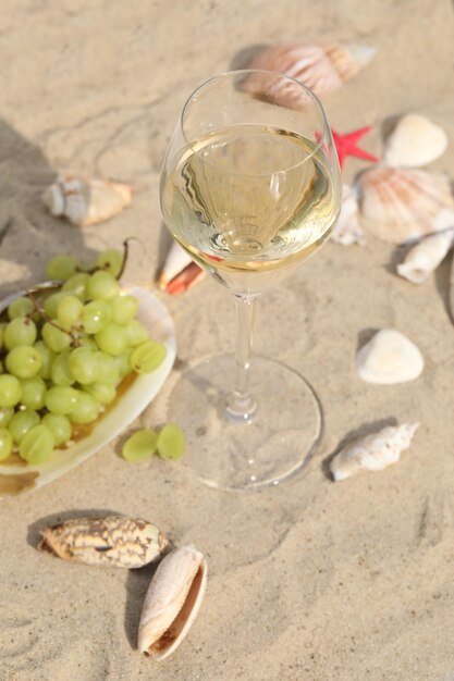 glass of white wine on sand as background with shells