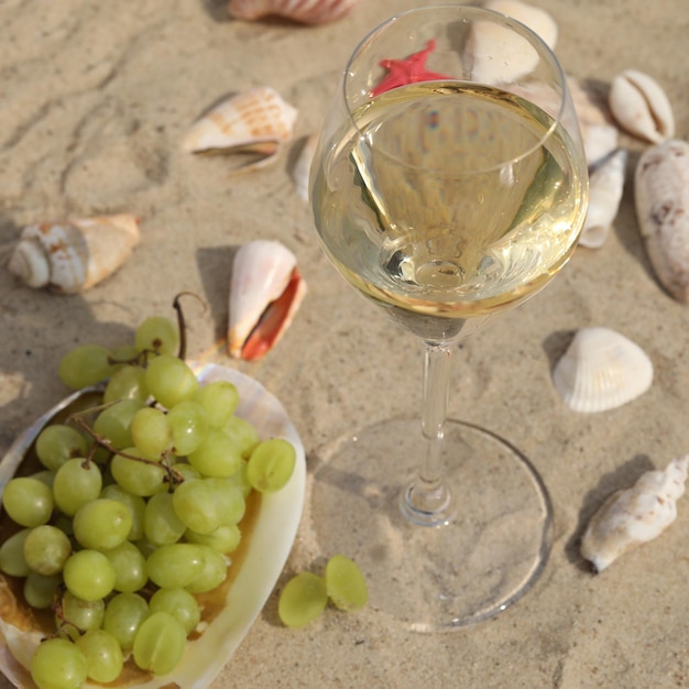 glass of white wine on sand as background with shells