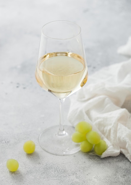 Glass of white wine with grapes and linen cloth on light table background