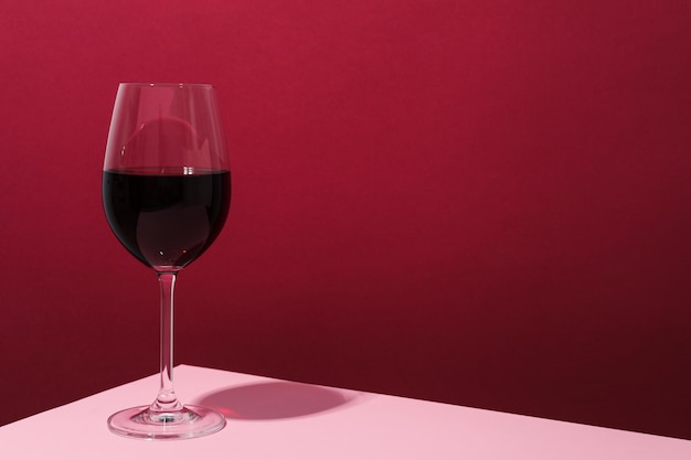 Glass of wine on pink table against crimson background space for text