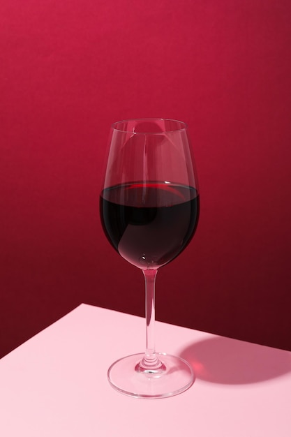 Glass of wine on pink table against crimson background