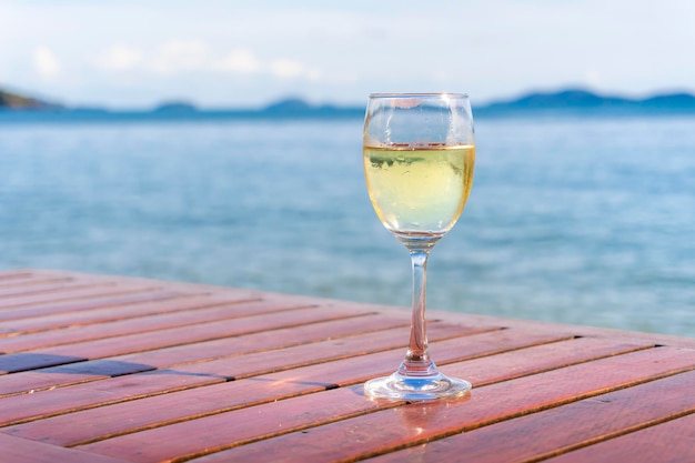 A glass of wine placed on a wooden table by the sea and warm sunlight