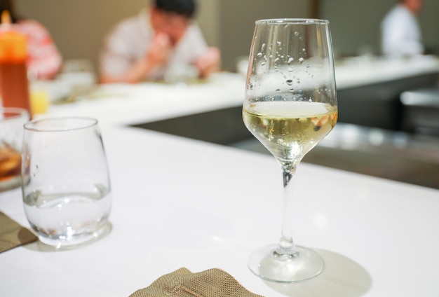 A glass of wine sits on a table with a man in the background.