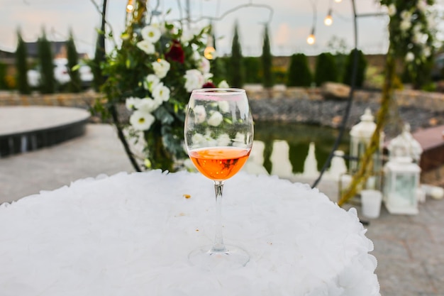 Glass of wine standing on the small tables outdoors White flowers arch at the wedding ceremony on background Stylish decoration