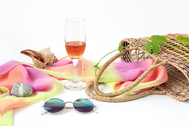 Photo a glass of wine a wicker basket with a light scarf sunglasses a shell on a light background  the concept of a pleasant summer holiday