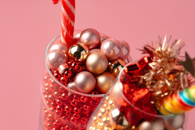 Glass with Christmas decorations on pink pastel background