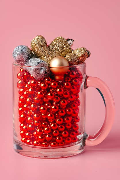 Glass with christmas decorations on pink pastel background