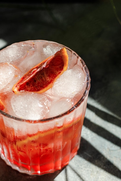 Glass with cold mineral water with blood oranges and ice cubes on concrete background Tropical palm leaf shadow Sunlight and shadow background