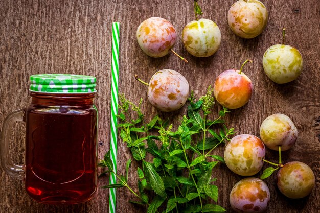 Glass with fresh plum juice and green mint on vintage wooden background