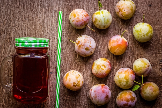 Glass with fresh plum juice on vintage wooden background