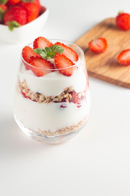 Glass with granola yogurt and fresh strawberries on white table Healthy breakfast bowl concept